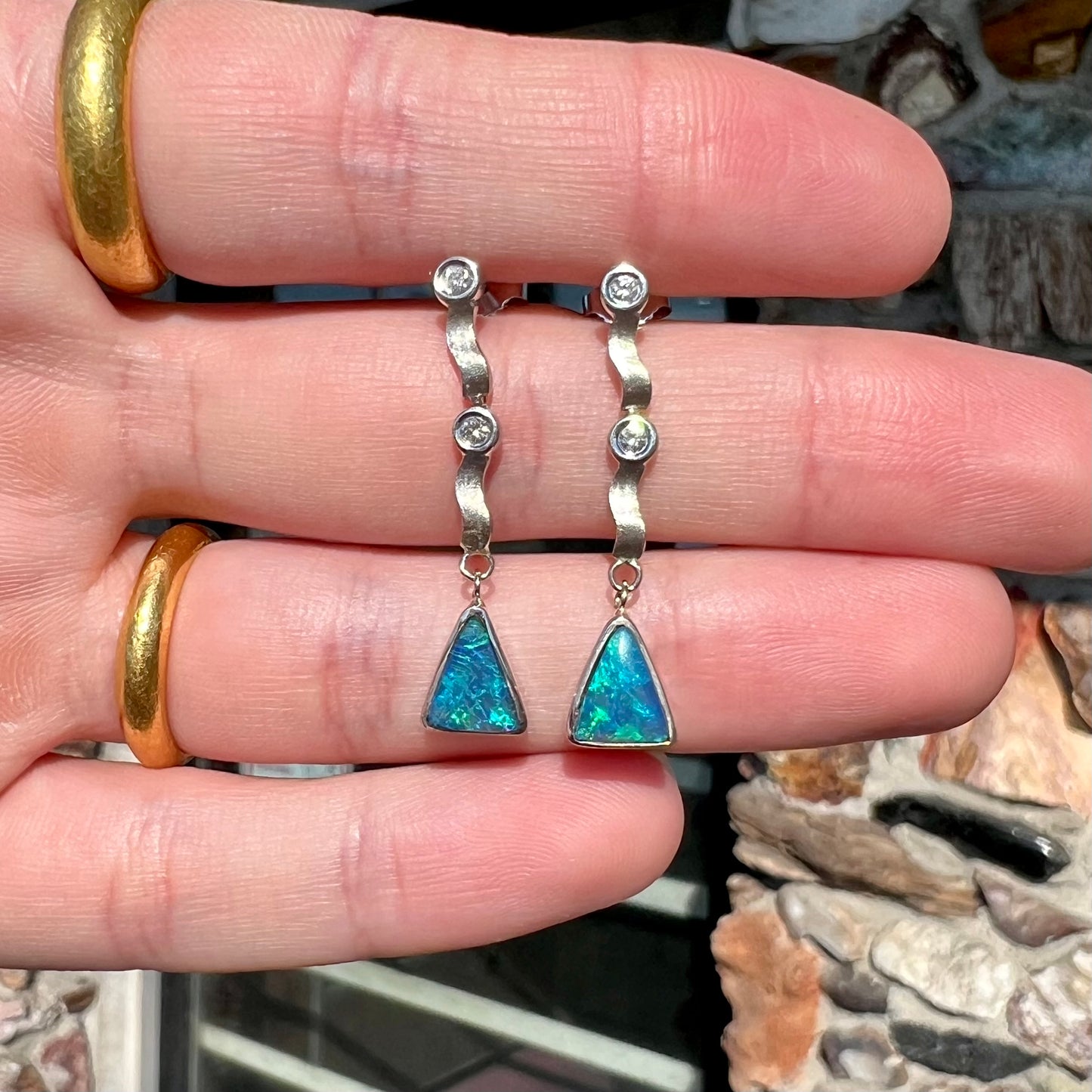 A pair of white gold earrings set with triangle cut natural black opals and round diamond accents.