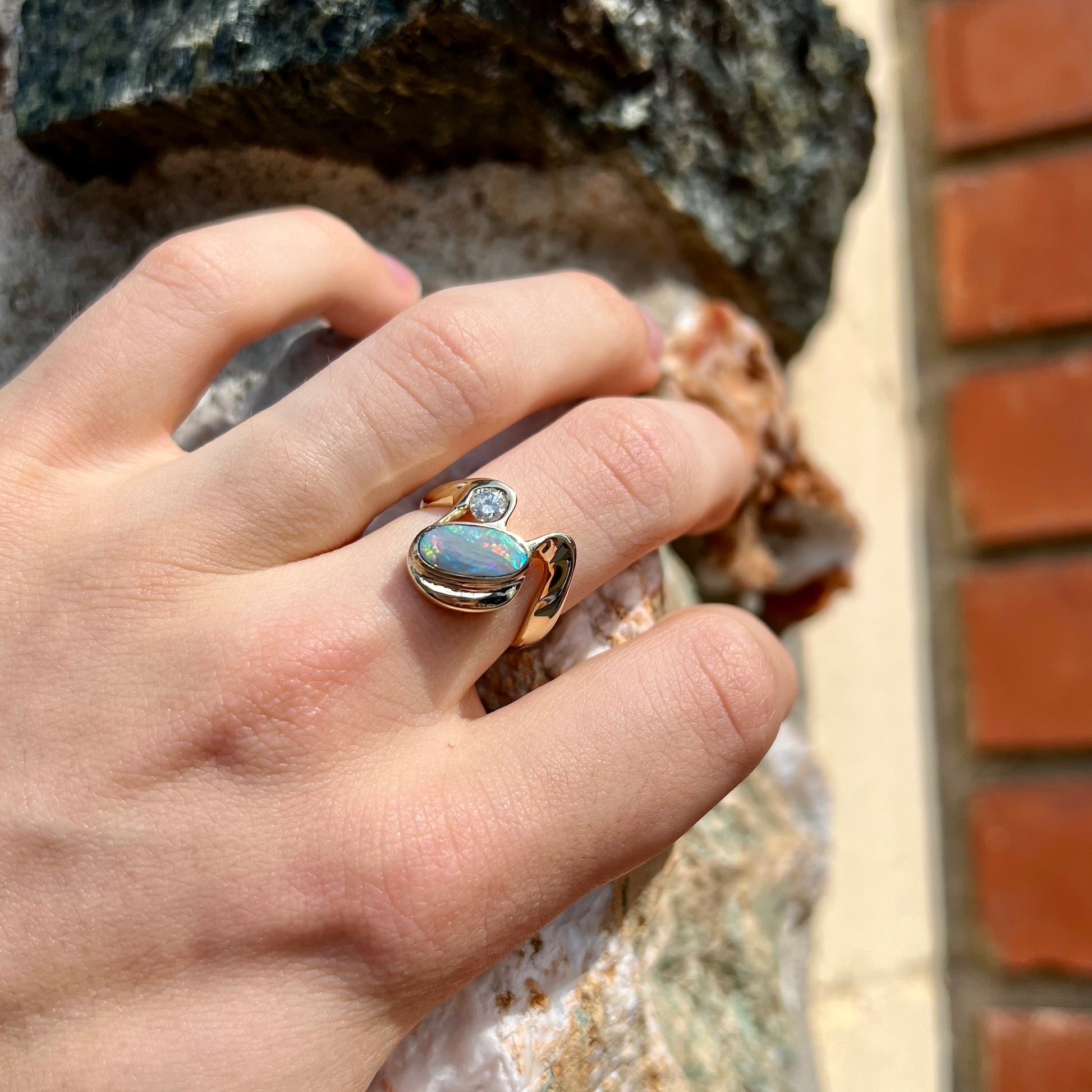 A ladies' yellow gold, bezel set ring mounted with a natural 1.15 carat black opal and round diamond.