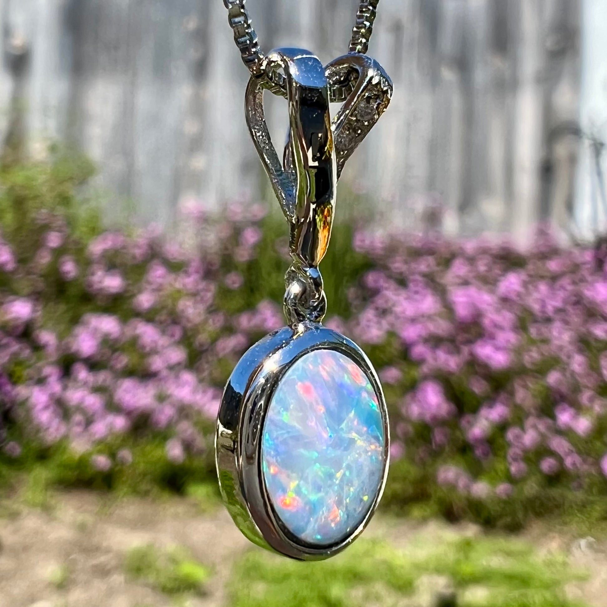 An oval cut black opal doublet necklace set in sterling silver with white zircon accent stones.