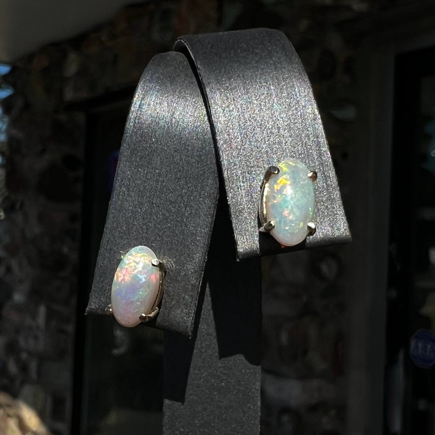A pair of natural, semi-black crystal opal stud earrings in yellow gold.  The opals are oval cabochon cut.