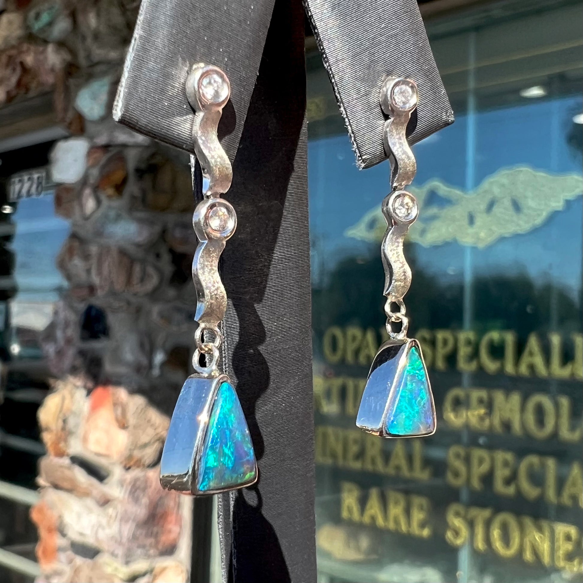 A pair of white gold earrings set with triangle cut natural black opals and round diamond accents.