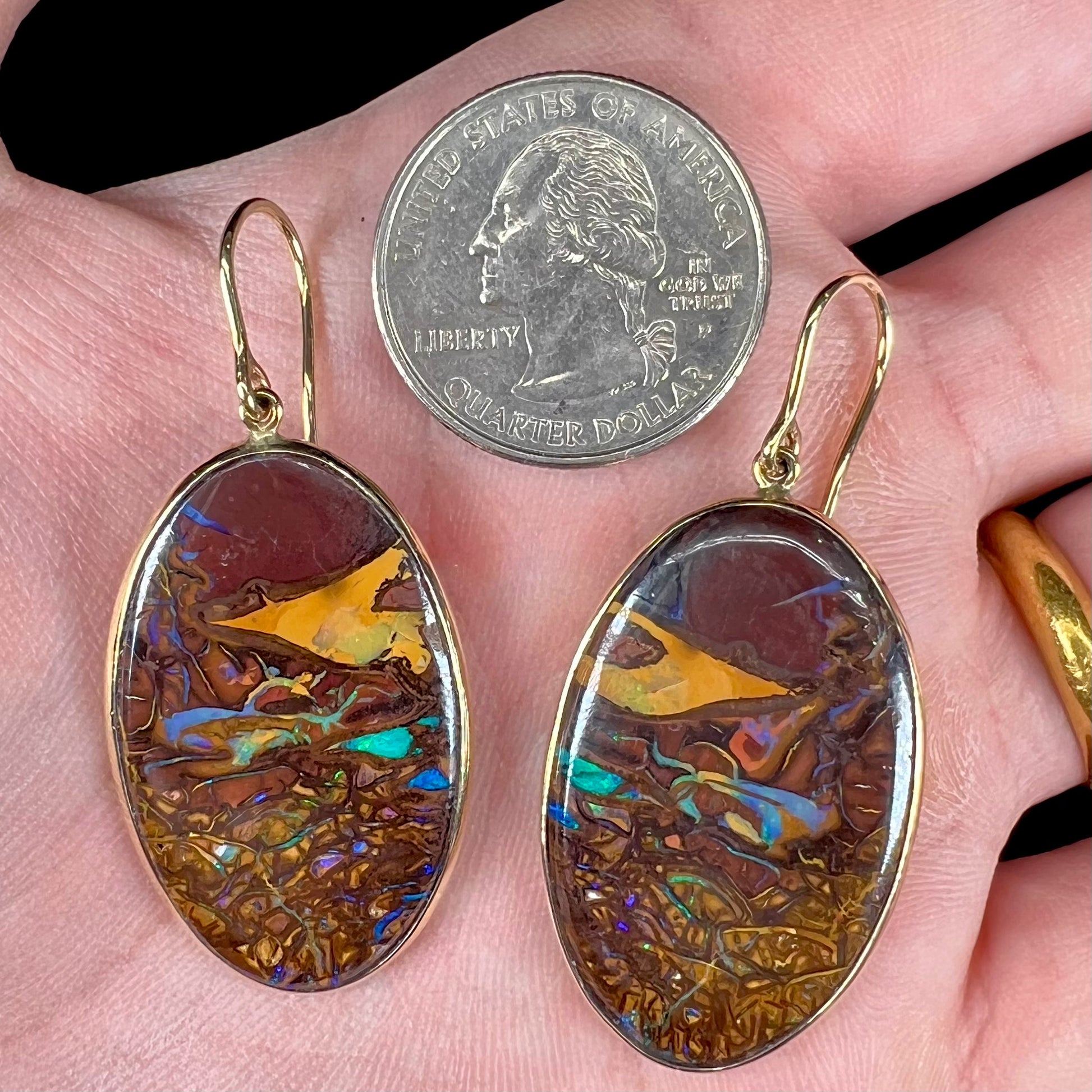 A pair of oval cut Koroit boulder opal dangle earrings in yellow gold bezel frames.  The opal exhibits a unique pattern and blue colors.