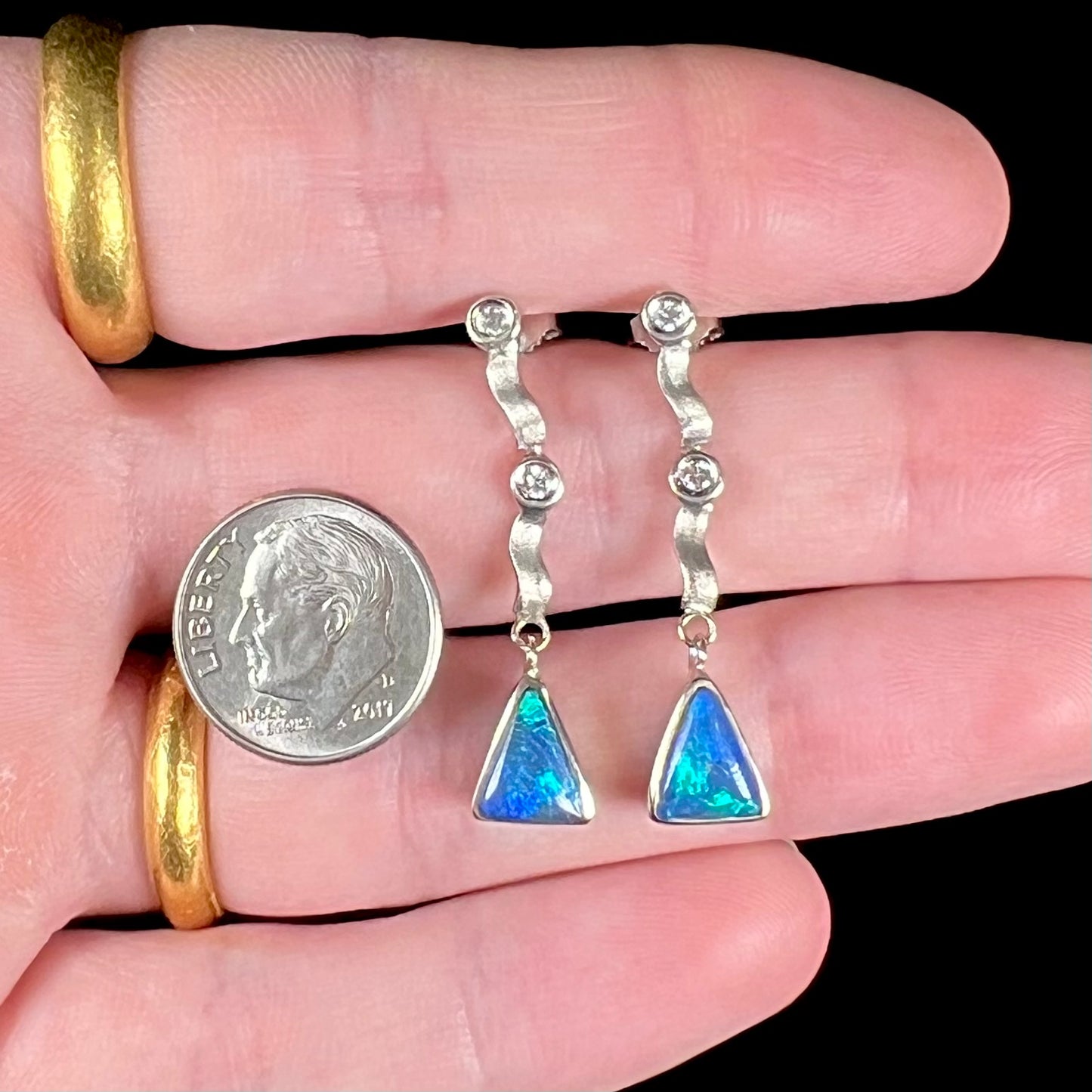 A pair of white gold earrings set with triangle cut natural black opals and round diamond accents.