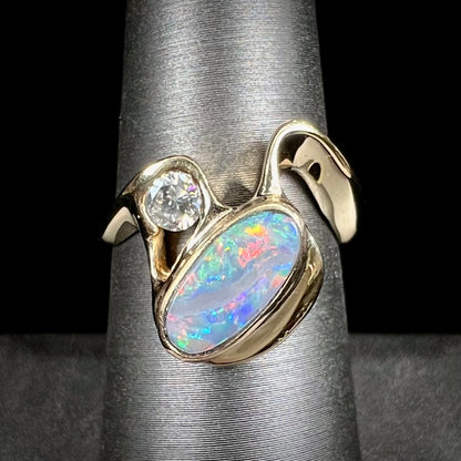 A ladies' yellow gold, bezel set ring mounted with a natural 1.15 carat black opal and round diamond.
