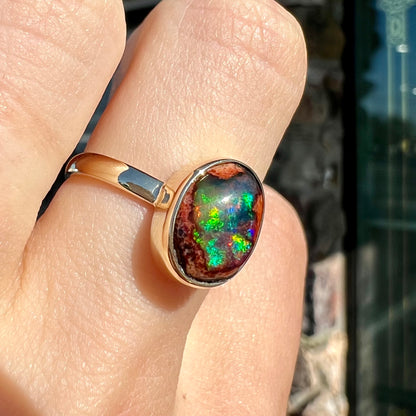 A ladies' yellow gold solitaire ring bezel set with an oval cabochon cut natural black Mexican cantera fire opal stone.
