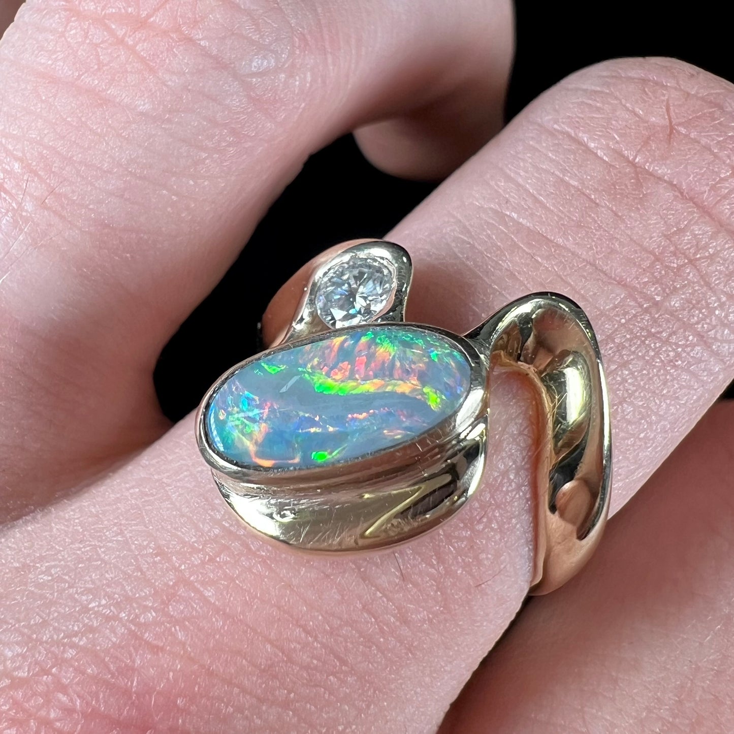 A ladies' yellow gold, bezel set ring mounted with a natural 1.15 carat black opal and round diamond.