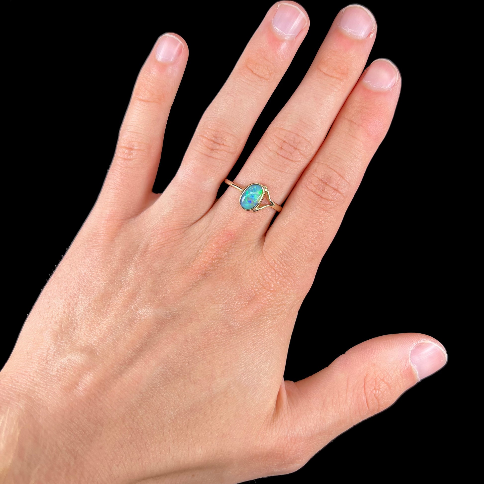 A ladies' oval cut black crystal opal solitaire ring handmade with a single split shank in yellow gold.