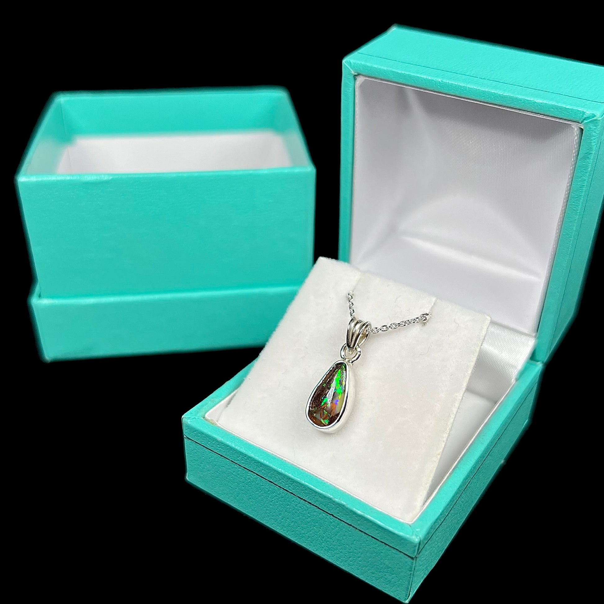 A natural, pear shaped Australian boulder opal with blue, purple, and green colors bezel set into a sterling silver necklace.