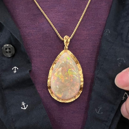 A ladies' natural, pear shaped, gray base Australian opal pendant set in 18 karat yellow gold.