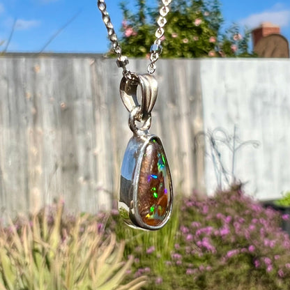 A pear shaped boulder opal necklace in sterling silver.  The opal has bright green and blue flashes.