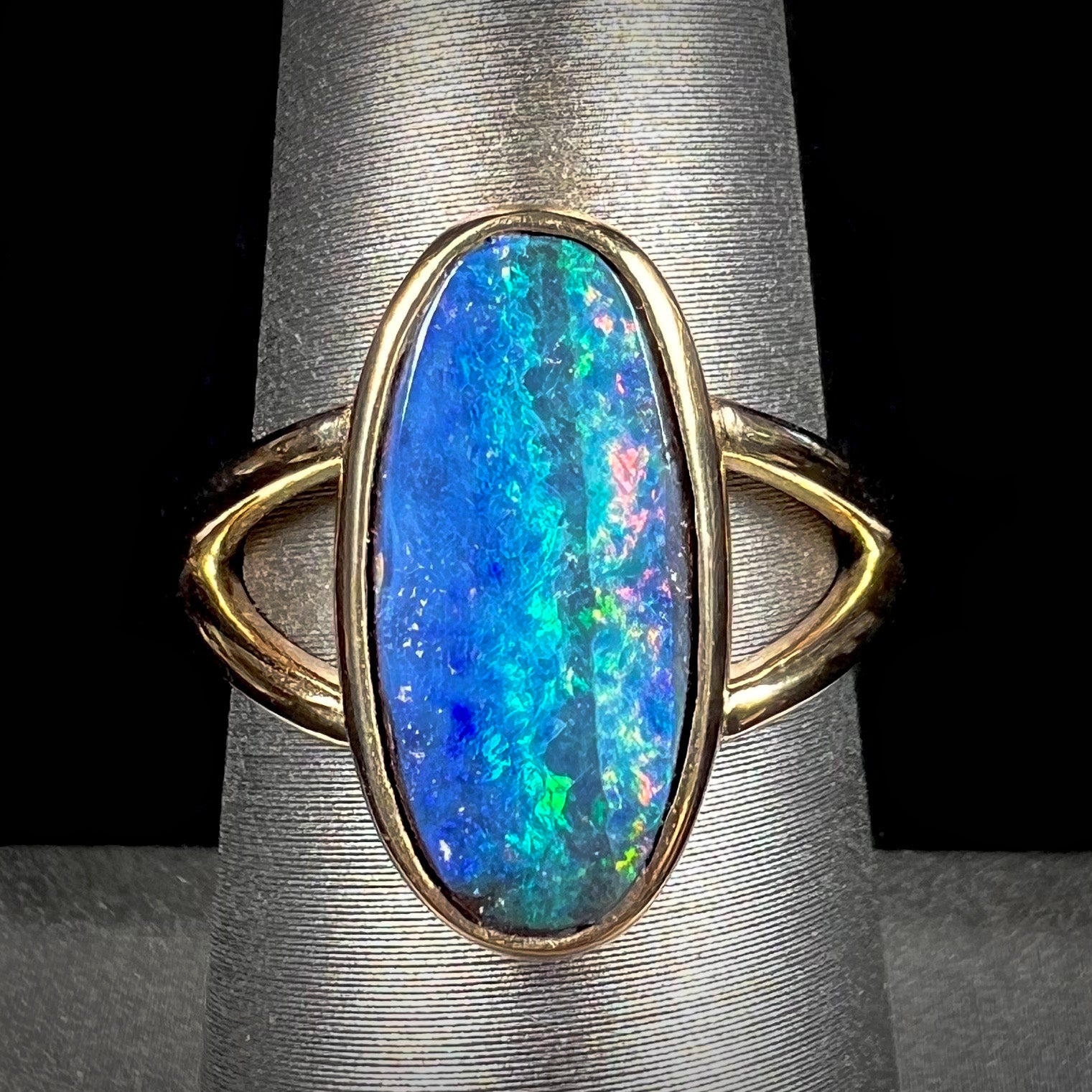 A ladies' yellow gold split shank solitaire ring set with a natural Australian black boulder opal.