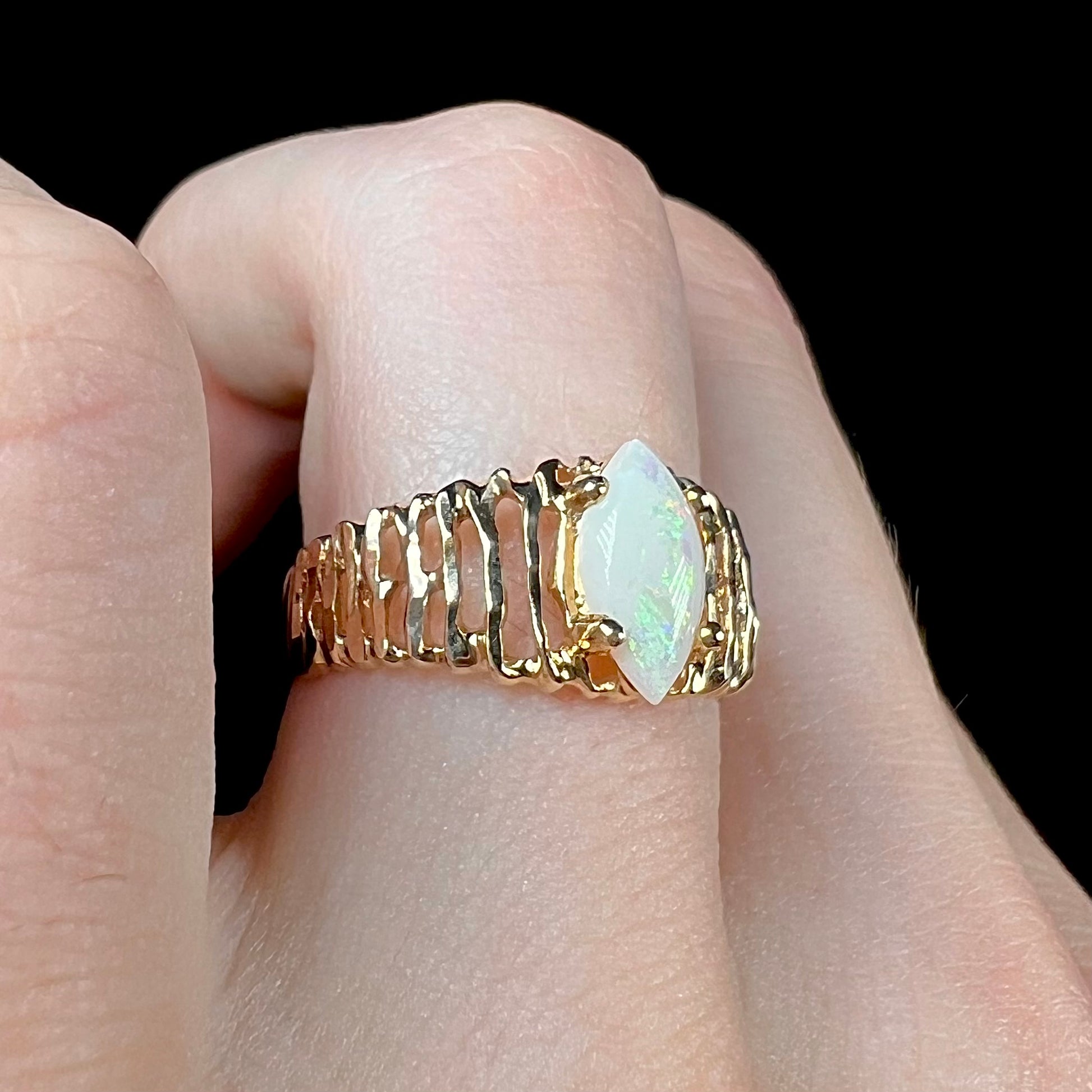 A ladies' yellow gold diamond-cut ring prong set with a natural, marquise cut white opal stone.