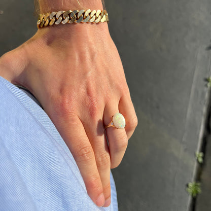 A ladies' yellow gold ring set with two diamonds and an oval cut natural opal stone.