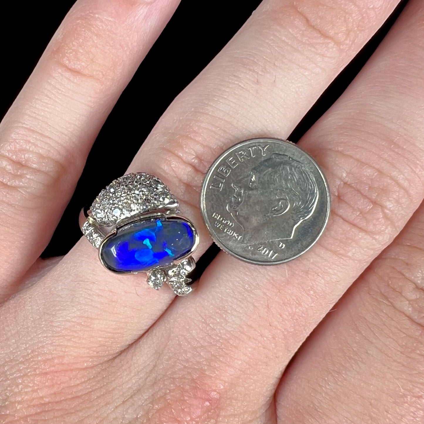 A platinum ring set with an oval cut black opal and round cut diamonds in a leaf design.