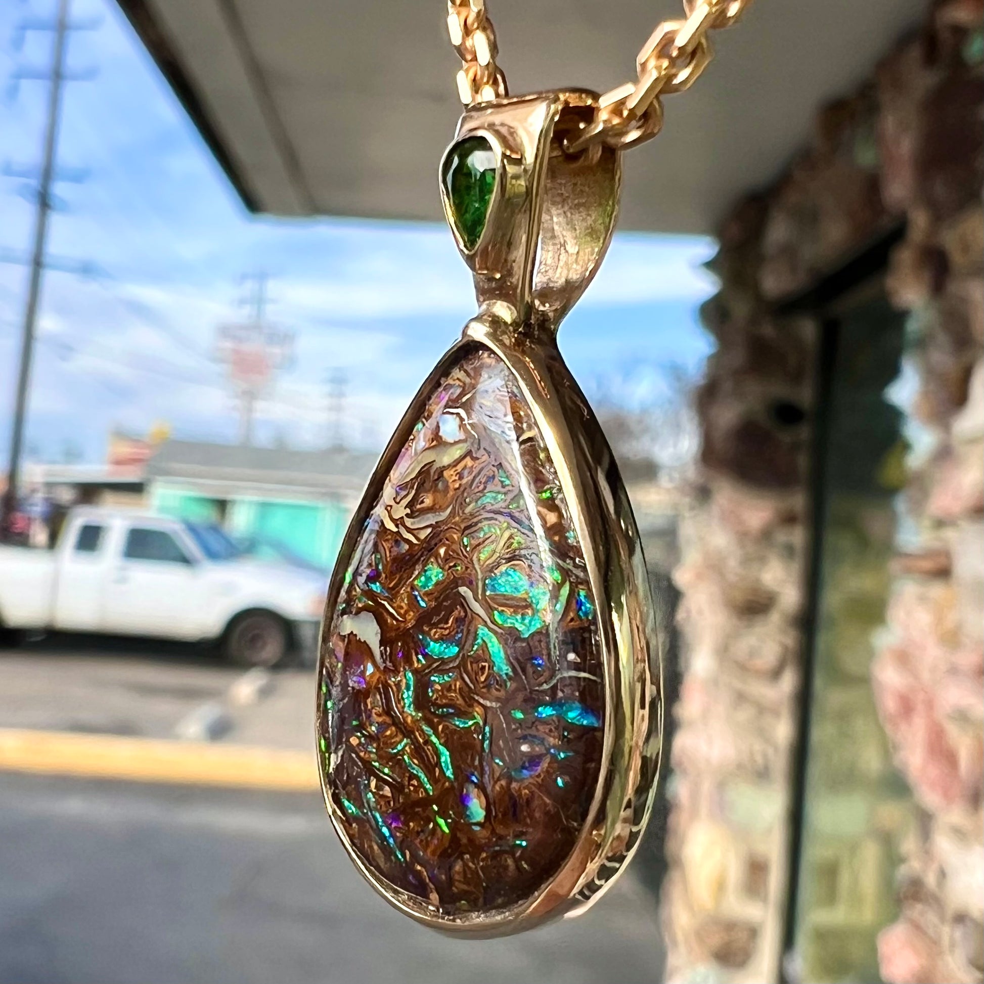 A ladies' yellow gold pendant set with a natural Koroit, Australian boulder opal and a tsavorite garnet accent stone.