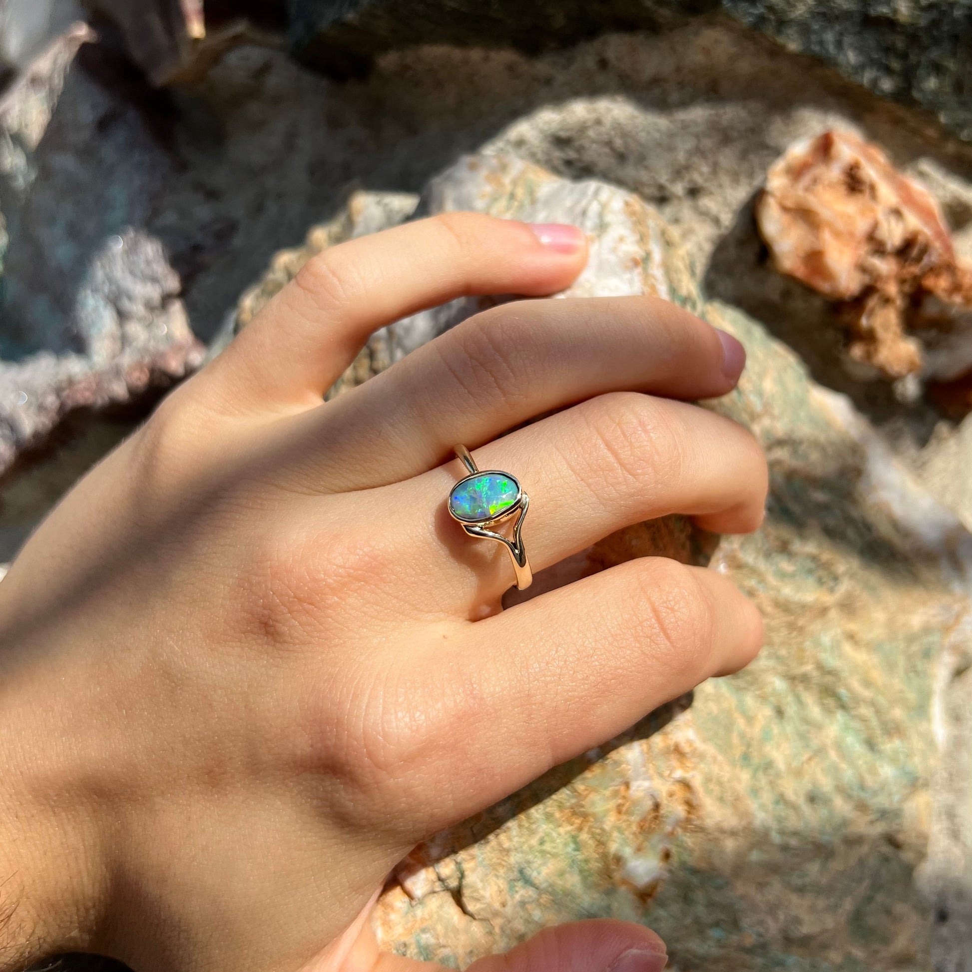 A ladies' oval cut black crystal opal solitaire ring handmade with a single split shank in yellow gold.