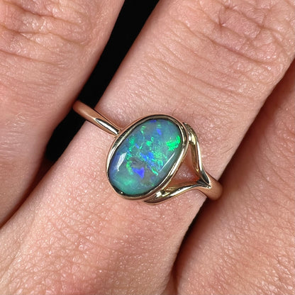 A ladies' oval cut black crystal opal solitaire ring handmade with a single split shank in yellow gold.