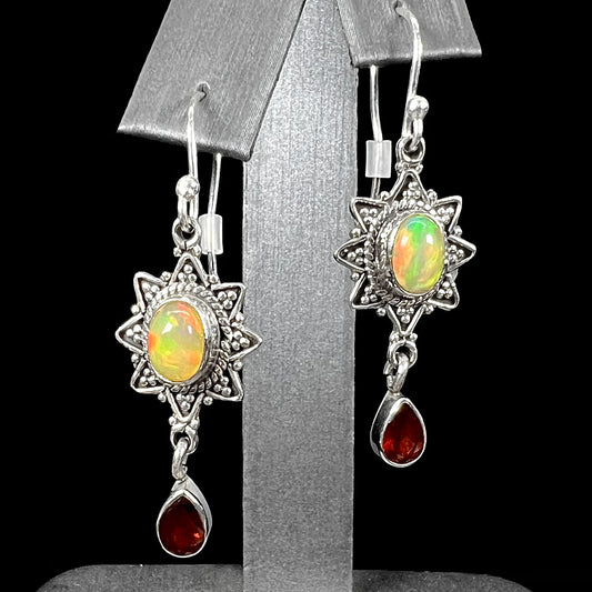 A pair of sterling silver star design dangle earrings set with Ethiopian fire opals and pear shaped red garnet accents.