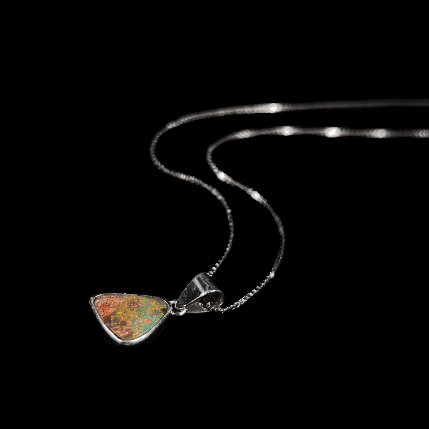 A sterling silver boulder opal necklace on a box chain.  The opal twinkles bright red, green, and blue colors.