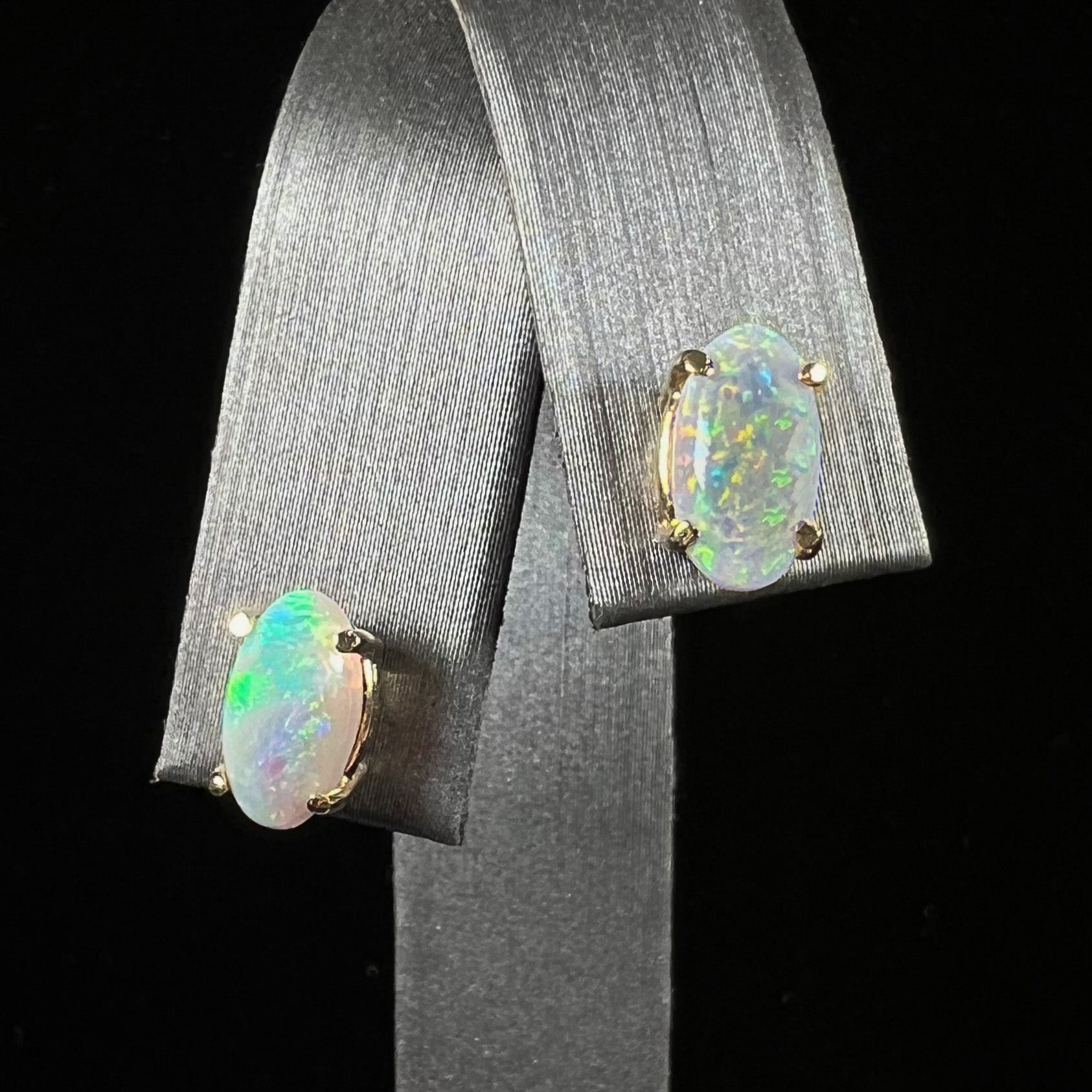 A pair of natural, semi-black crystal opal stud earrings in yellow gold.  The opals are oval cabochon cut.
