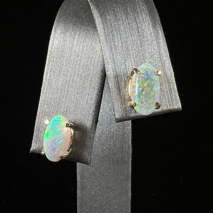 A pair of natural, semi-black crystal opal stud earrings in yellow gold.  The opals are oval cabochon cut.