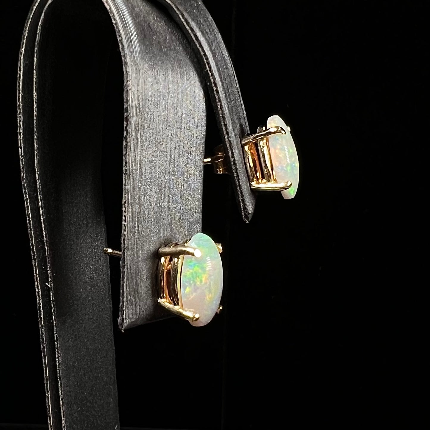 A pair of natural, semi-black crystal opal stud earrings in yellow gold.  The opals are oval cabochon cut.