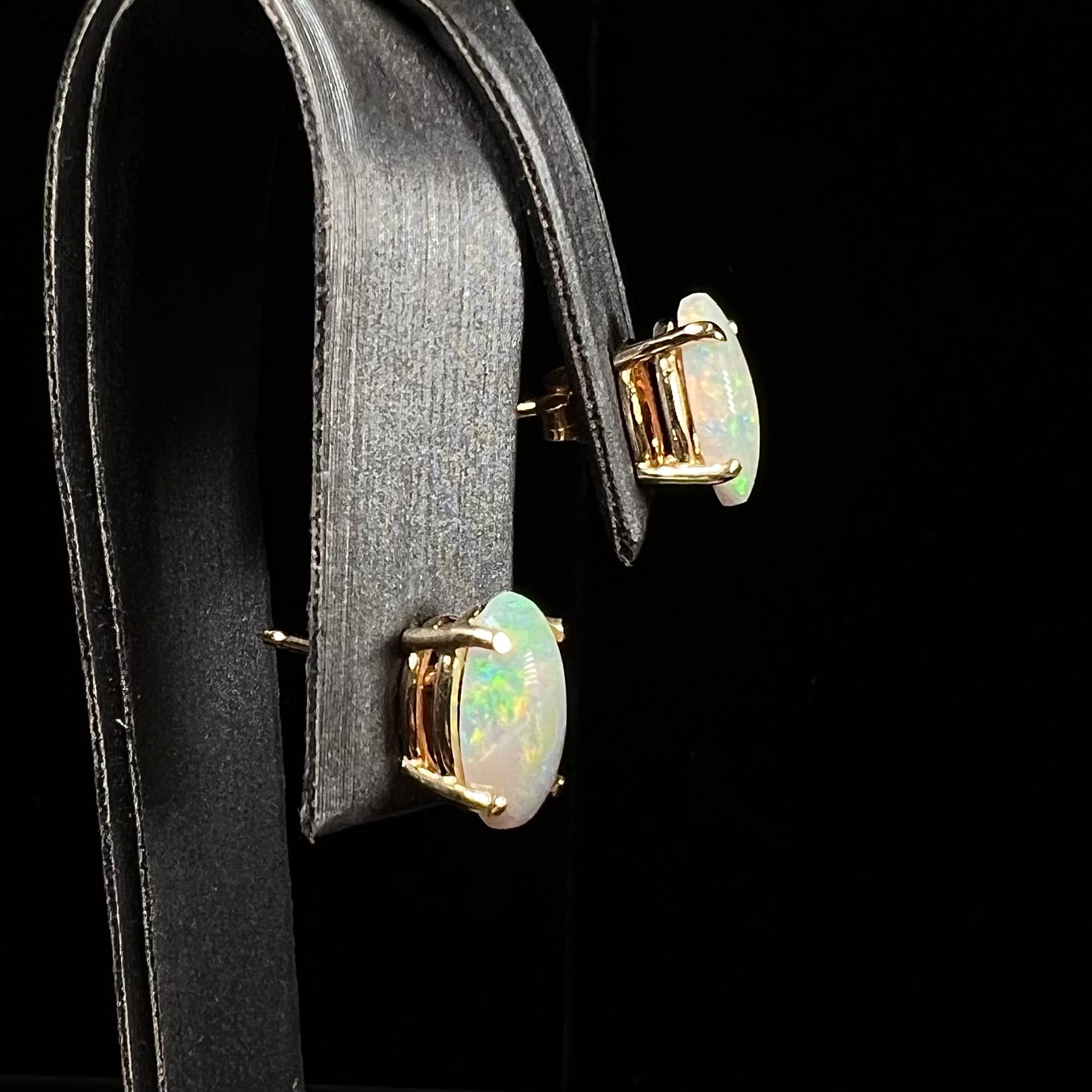 A pair of natural, semi-black crystal opal stud earrings in yellow gold.  The opals are oval cabochon cut.