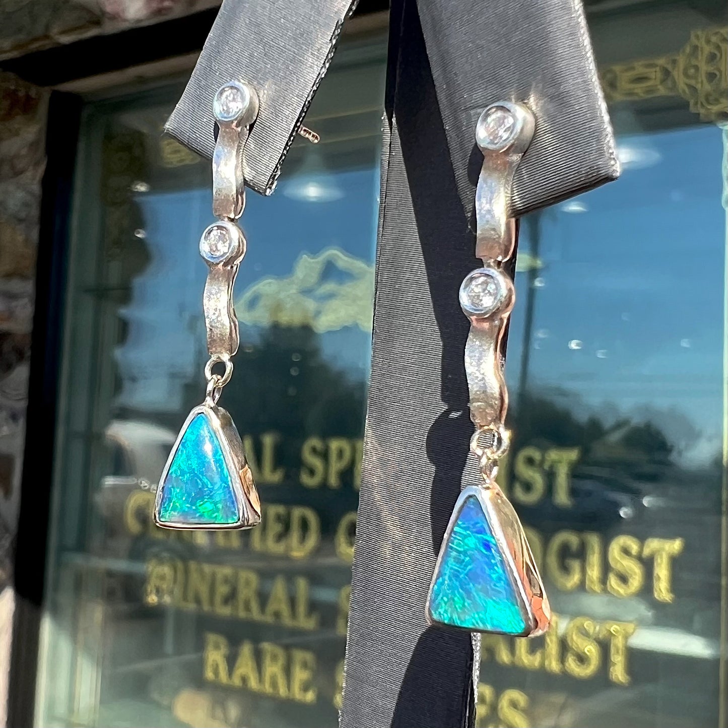 A pair of white gold earrings set with triangle cut natural black opals and round diamond accents.