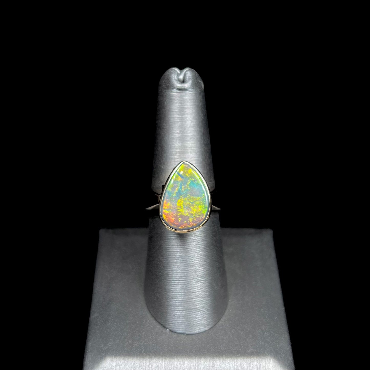 A large ladies' yellow gold solitaire ring set with a natural, pear shaped black crystal opal.  The opal has green and orange fire.