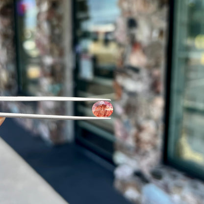 A loose, oval cut oregon sunstone.  The gem is reddish orange with a green secondary color.