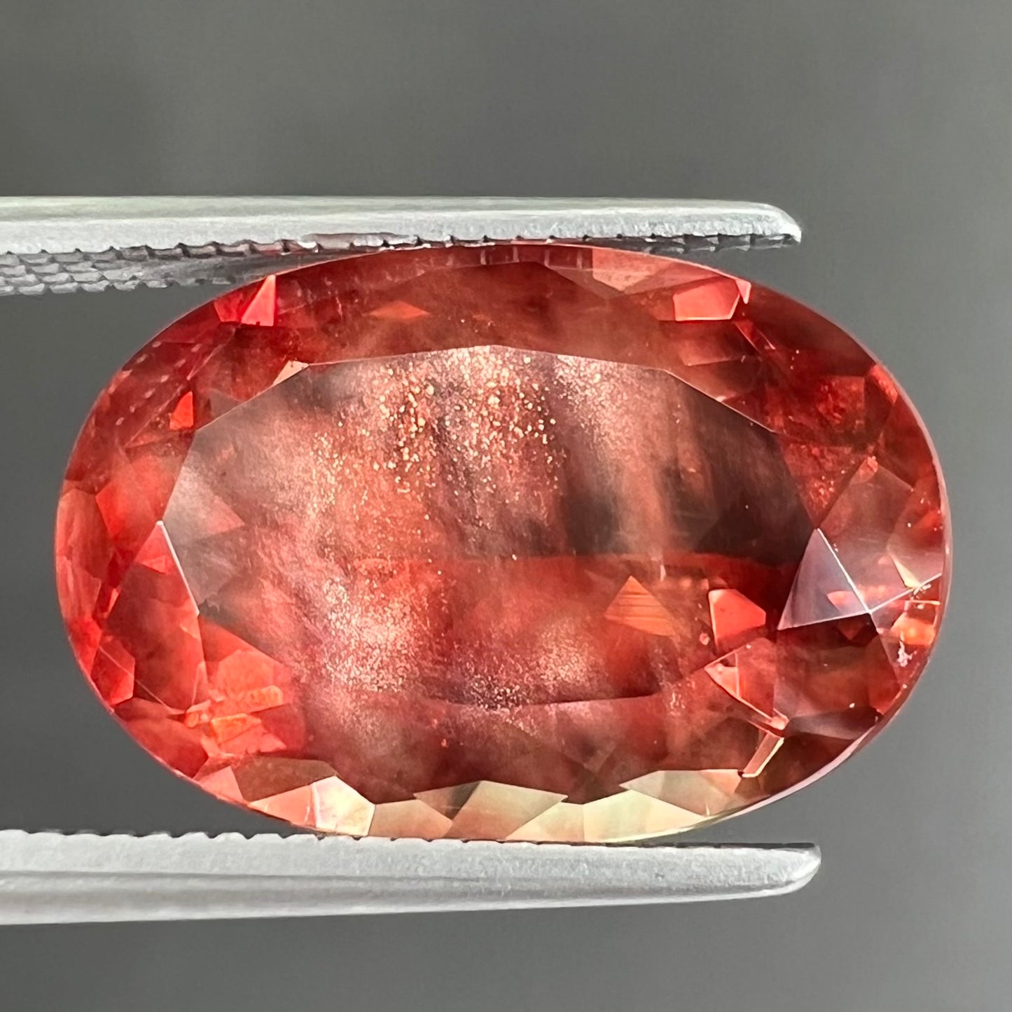 A faceted, oval cut sunstone.  The stone is red-orange color with a bright schiller flash.
