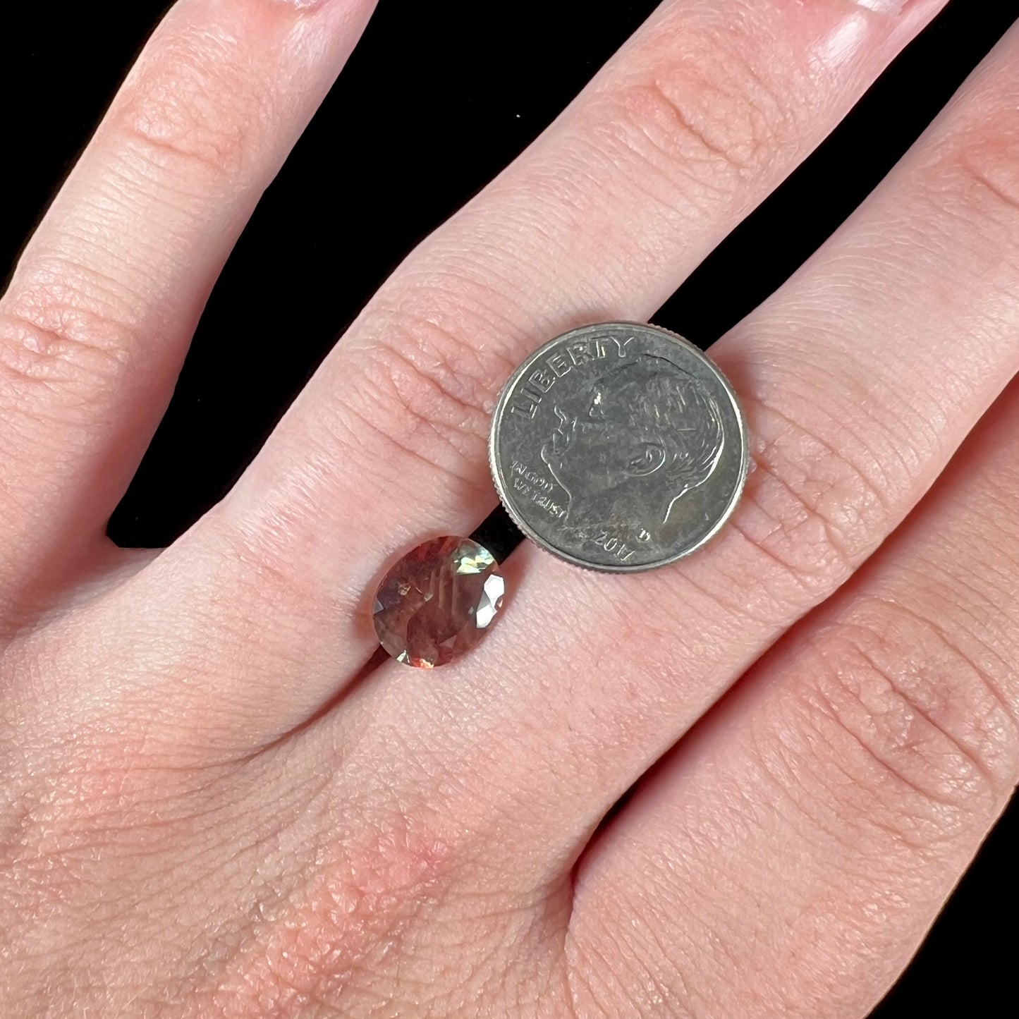 A loose, oval cut oregon sunstone.  The gem is reddish orange with a green secondary color.