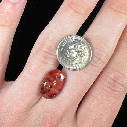 A faceted, oval cut sunstone.  The stone is red-orange color with a bright schiller flash.