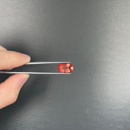 A faceted, oval cut sunstone.  The stone is red-orange color with a bright schiller flash.