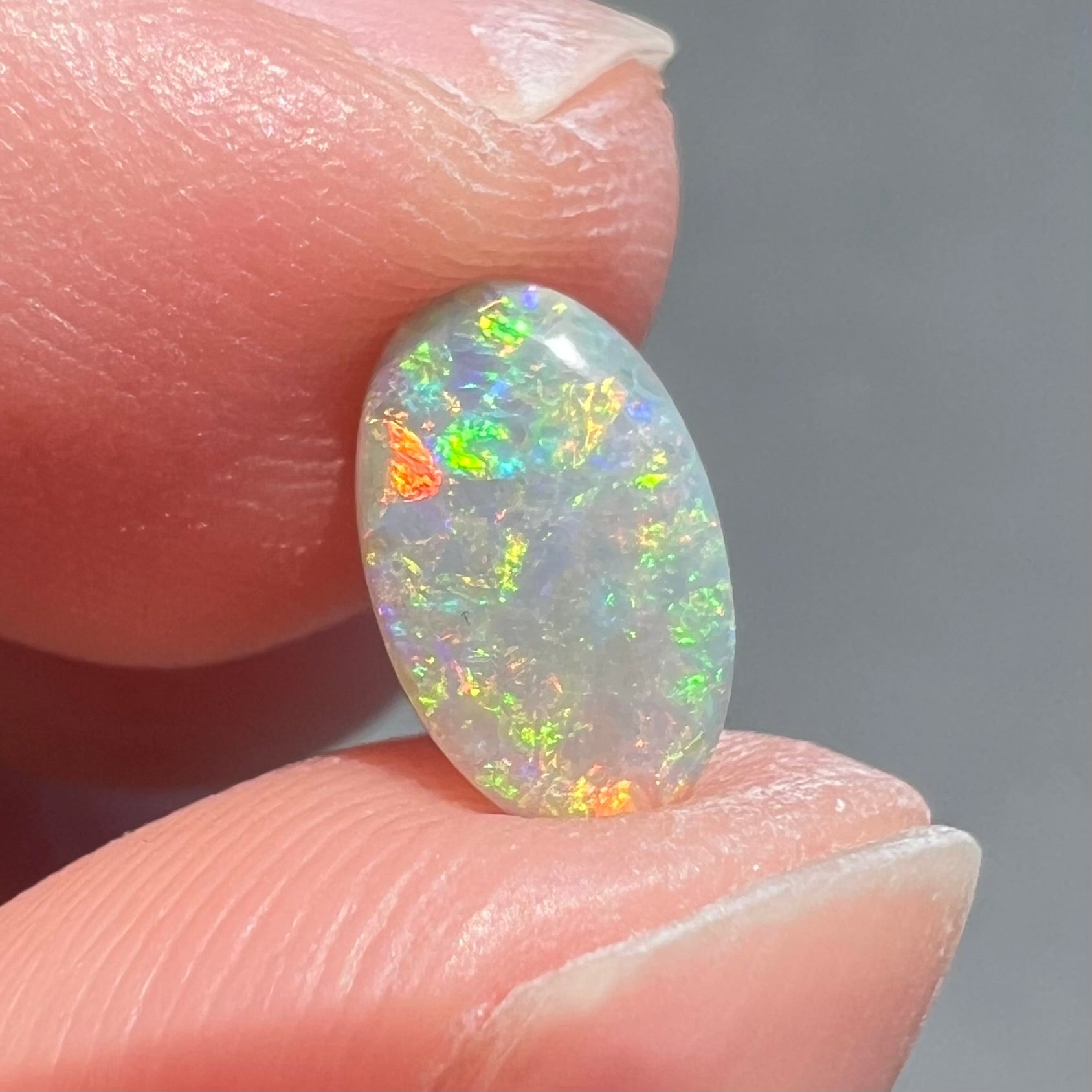 A loose, oval cabochon cut semi-black opal stone from Lightning Ridge, Australia.