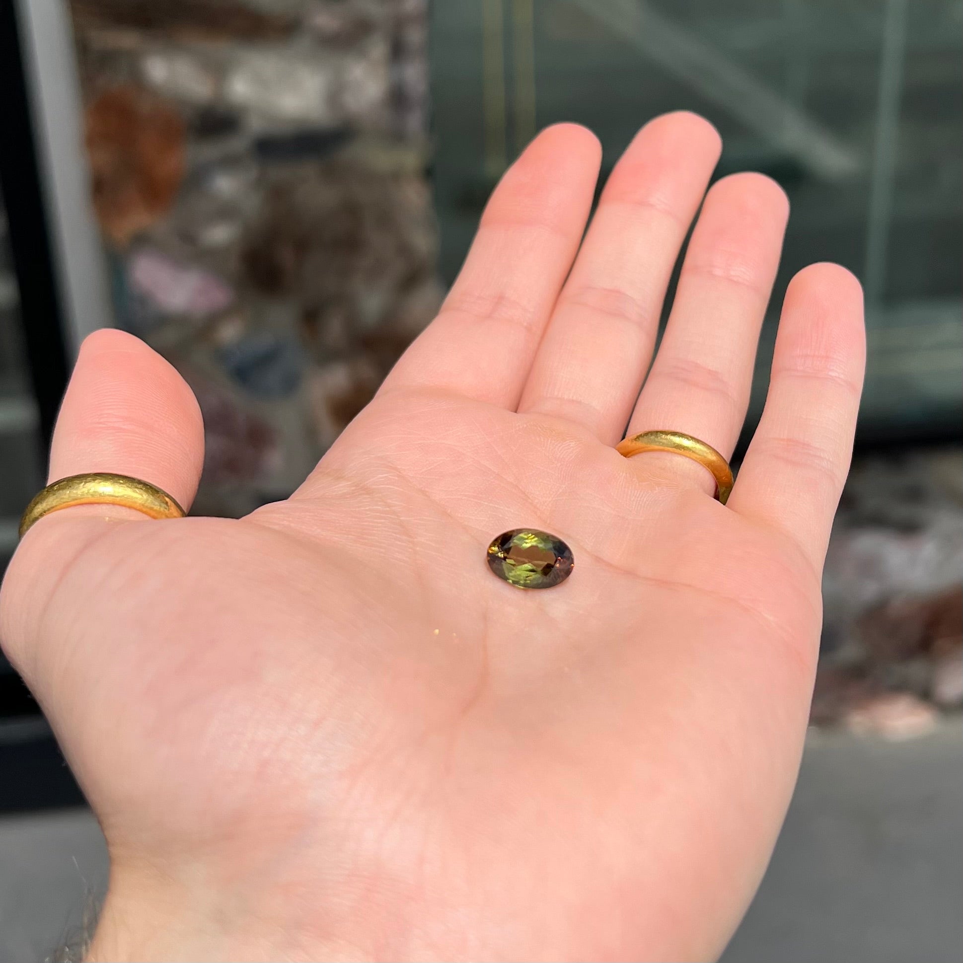 A loose, faceted oval cut andalusite gemstone.  The stone shows brown and green colors.
