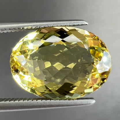 A faceted oval cut golden beryl gemstone.  The stone is a greenish light yellow.