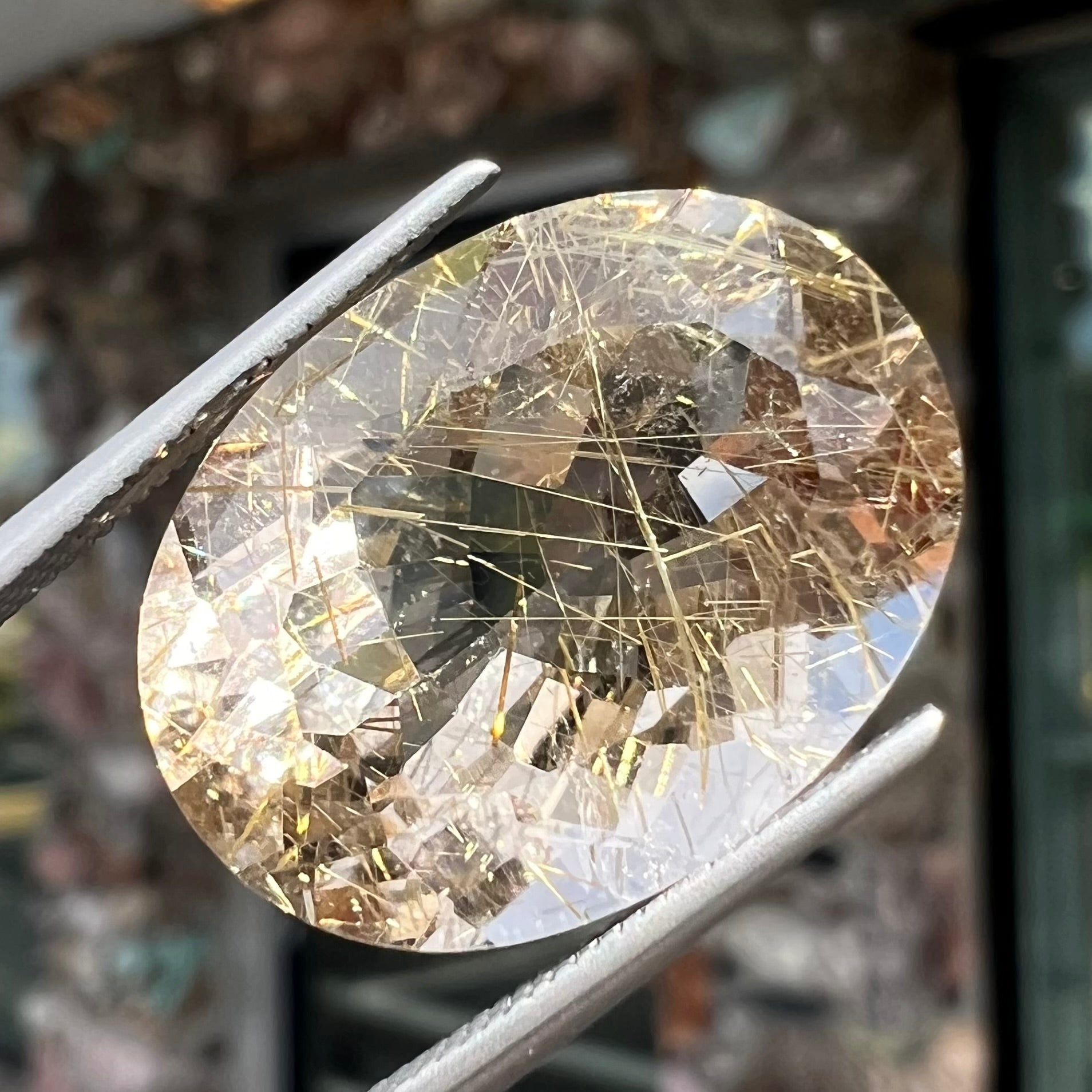 A faceted oval cut rutilated quartz gemstone.  The stone is smoky color with golden rutile needle inclusions.