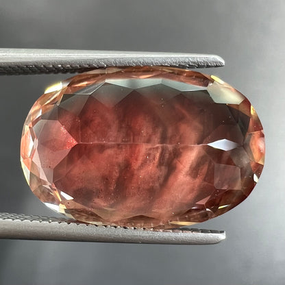 A faceted, oval cut sunstone.  The stone is red-orange color with a bright schiller flash.