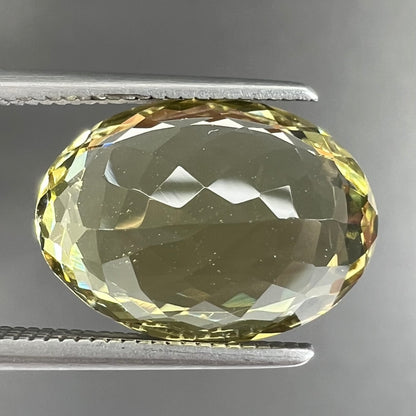 A faceted oval cut golden beryl gemstone.  The stone is a greenish light yellow.