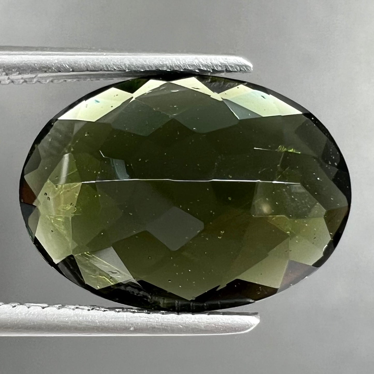 A faceted oval cut natural moldavite gemstone.