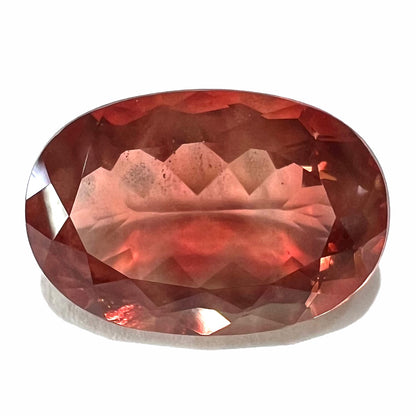 A faceted, oval cut sunstone.  The stone is red-orange color with a bright schiller flash.