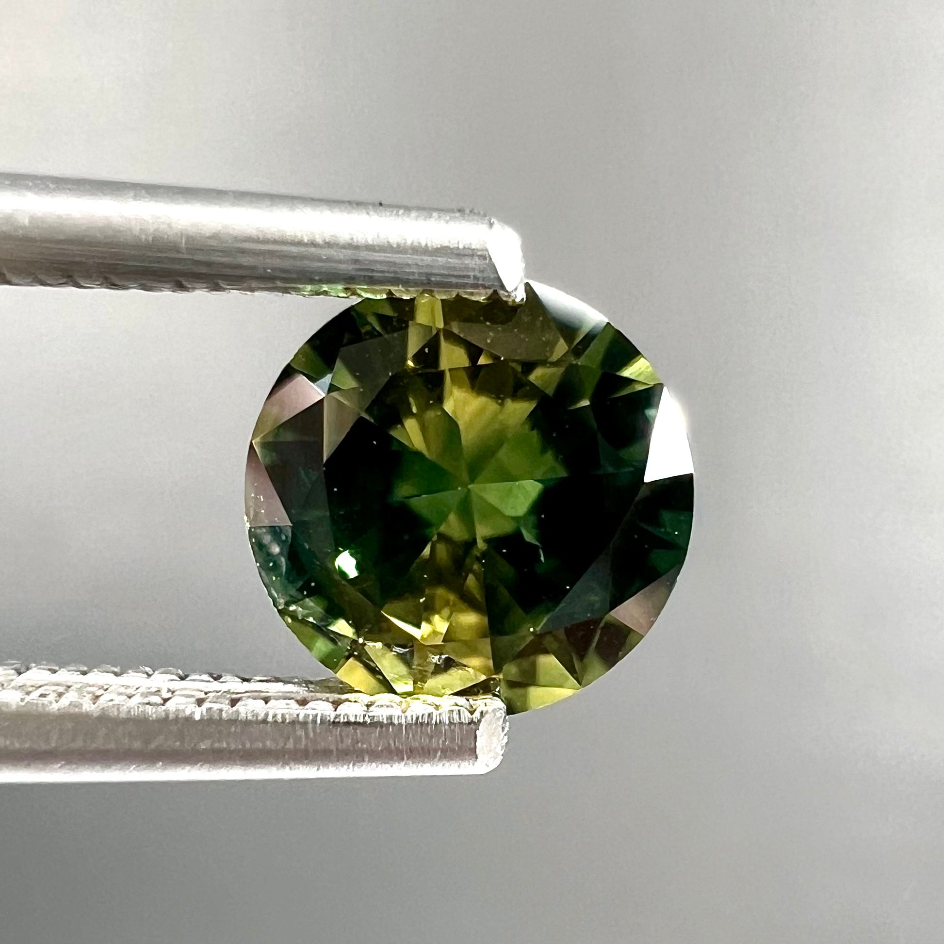 A loose, round brilliant cut Australian parti sapphire.  The stone shows colors of yellow, green, and blue.