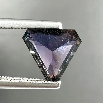 A loose, modified triangle cut parti sapphire gemstone.  The sapphire shows colors of blue, violet, purple, and gray.