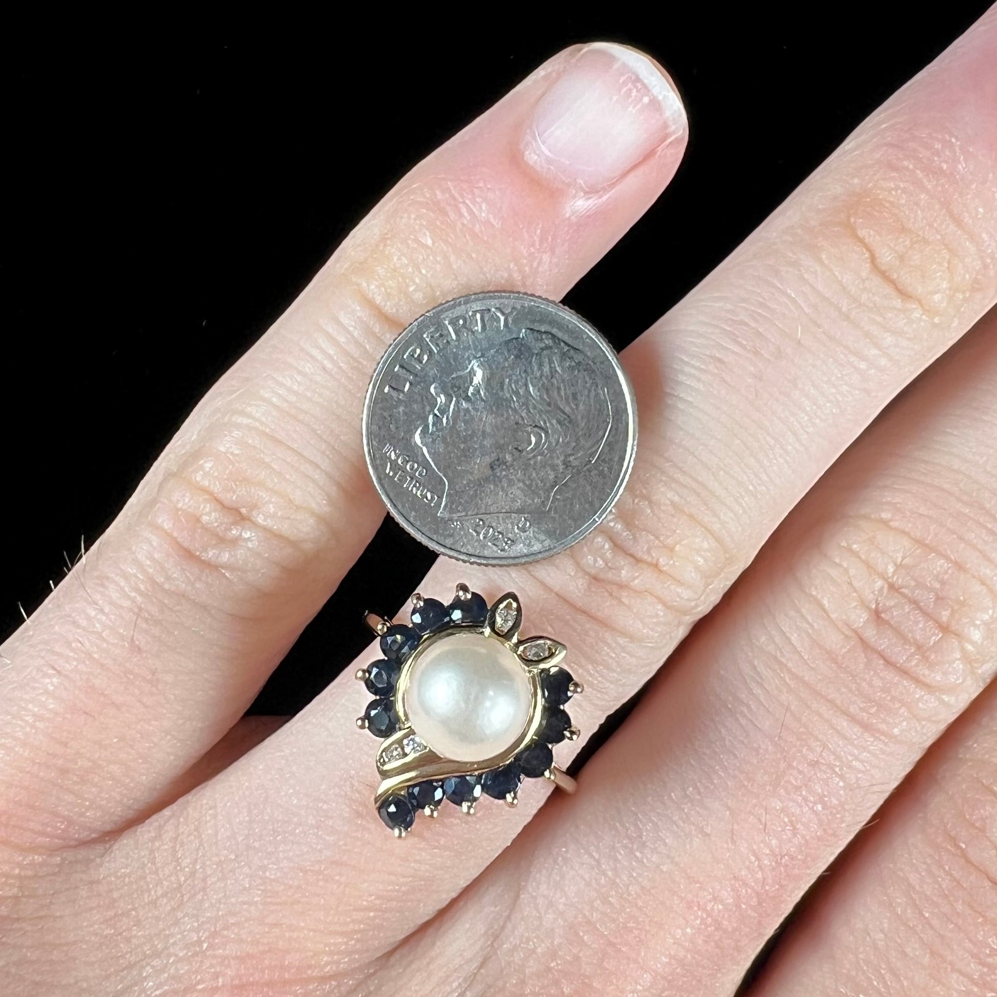 A yellow gold, heart shaped ring set with a freshwater pearl surrounded by blue sapphire and diamond accent stones.