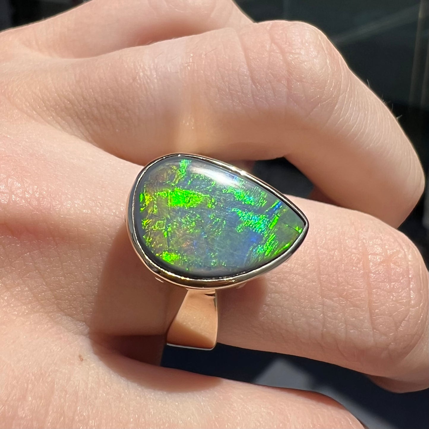 A large ladies' yellow gold solitaire ring set with a natural, pear shaped black crystal opal.  The opal has green and orange fire.