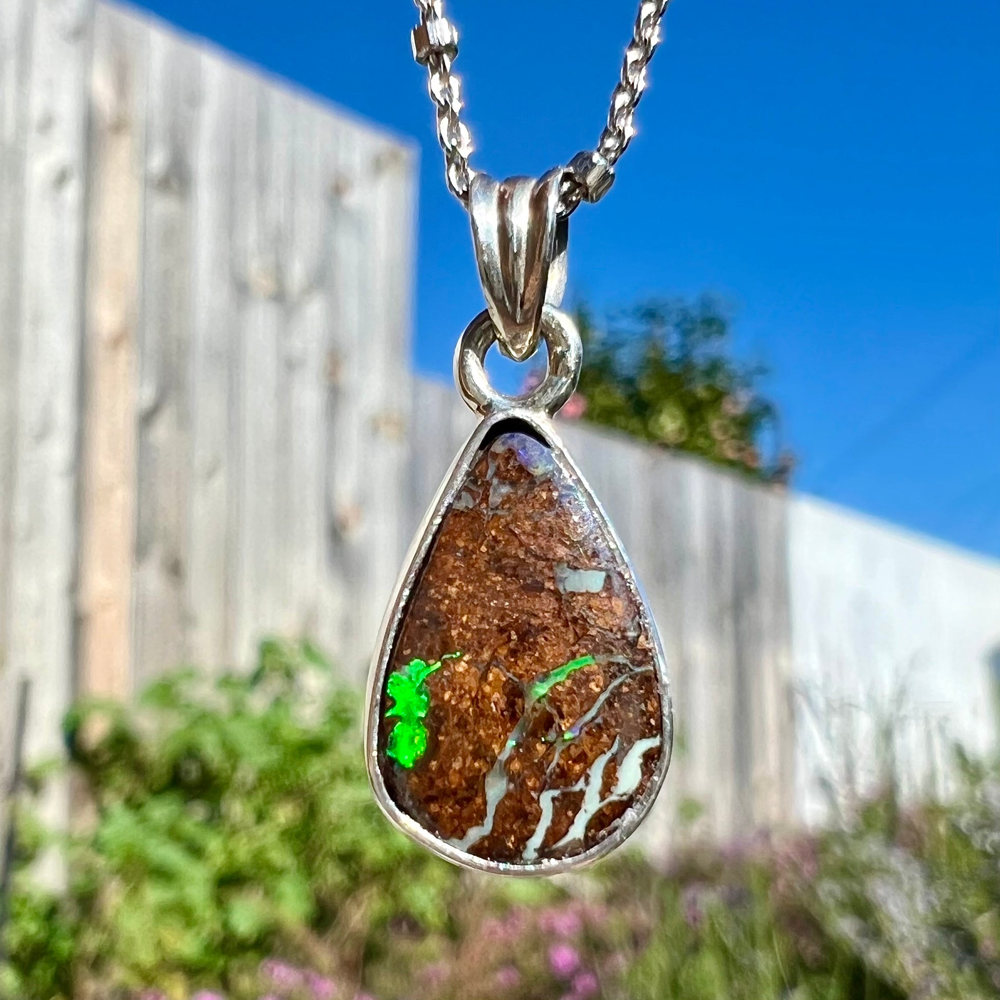 A pear shaped Australian boulder opal necklace in sterling silver.  The opal has bright flashes of green and blue colors.