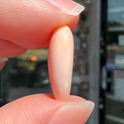 A loose, pear shaped pink Peruvian opal cabochon.  The opal has green play of color.