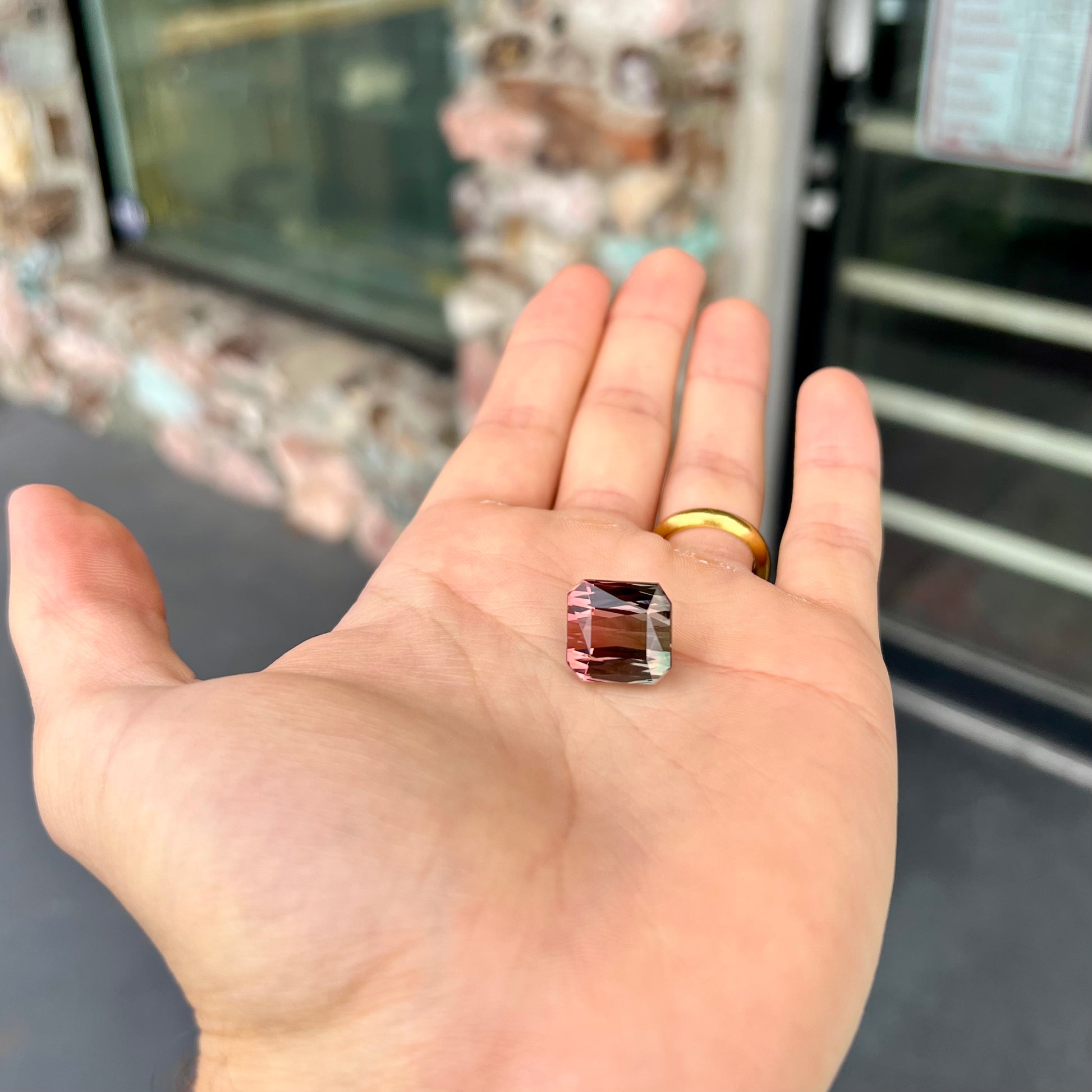 A loose, faceted modified emerald cut bicolor tourmaline gemstone.  The stone transitions from dark pink to dark green colors.