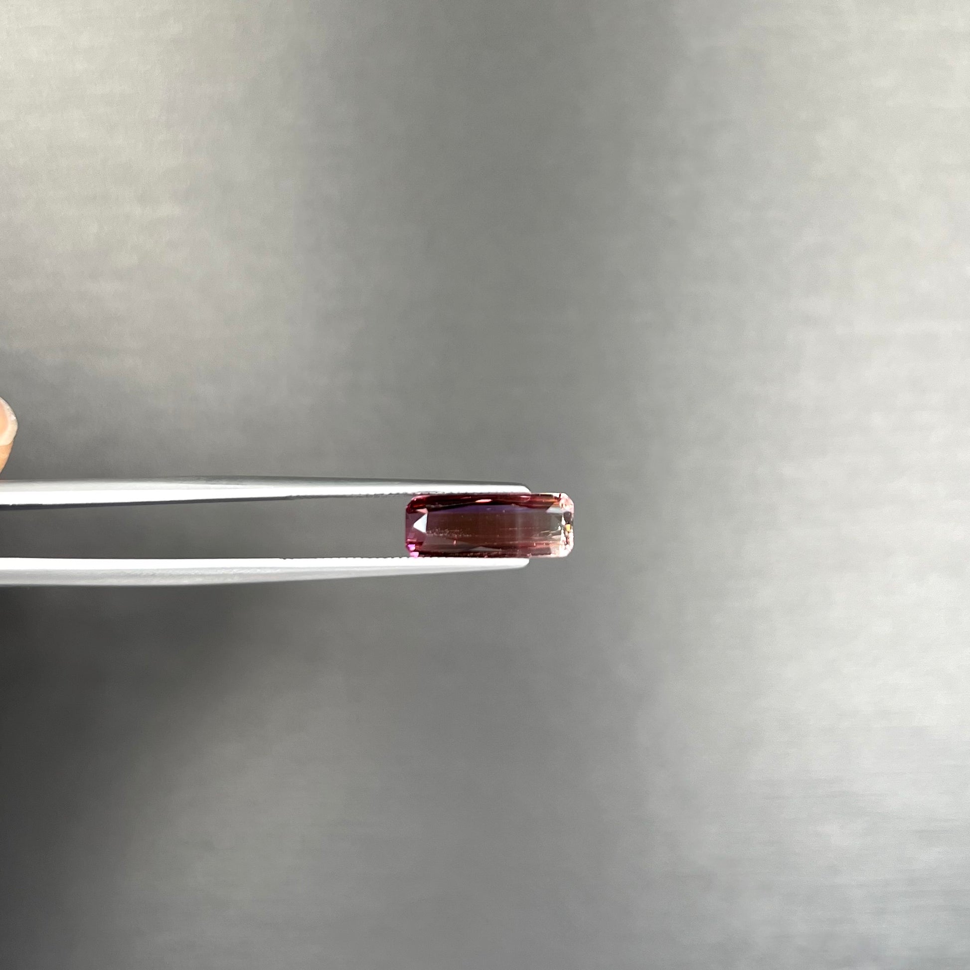 A loose, modified emerald cut tricolor tourmaline.  The stone transitions from pink to light pink to white colors.